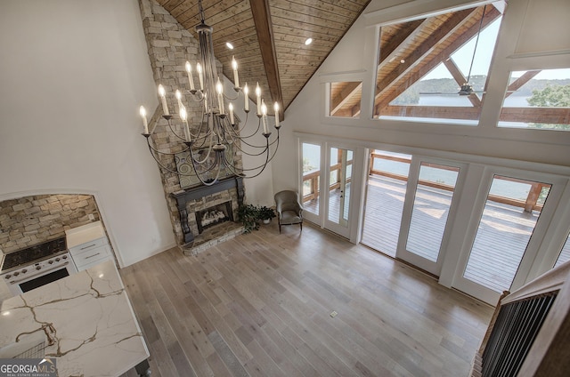 unfurnished living room with a stone fireplace, high vaulted ceiling, beamed ceiling, wooden ceiling, and light wood-type flooring