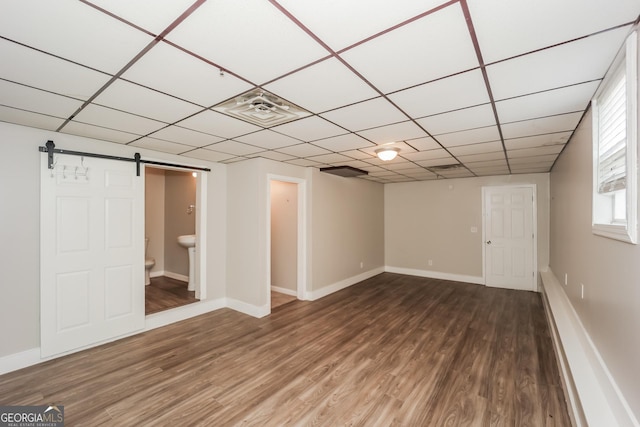 basement featuring hardwood / wood-style floors, a paneled ceiling, and a barn door