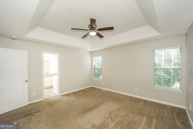 unfurnished bedroom with ceiling fan, multiple windows, connected bathroom, and a tray ceiling