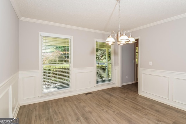 unfurnished dining area featuring a chandelier, hardwood / wood-style floors, a textured ceiling, and ornamental molding