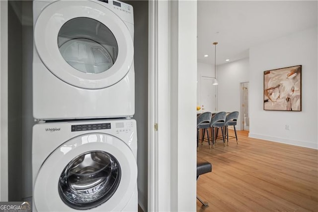 clothes washing area with hardwood / wood-style flooring and stacked washer and clothes dryer