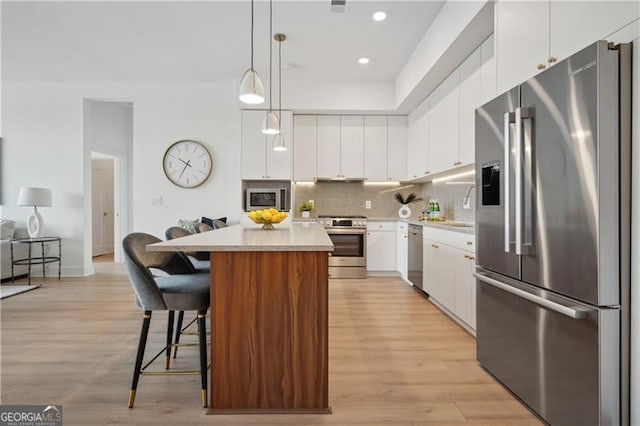 kitchen with a kitchen island, tasteful backsplash, white cabinetry, hanging light fixtures, and stainless steel appliances