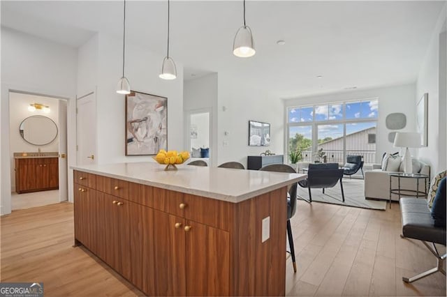 kitchen with a breakfast bar, pendant lighting, sink, a center island, and light wood-type flooring