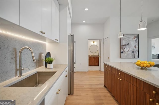 kitchen featuring pendant lighting, sink, light stone counters, and white cabinets