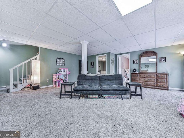 carpeted living area featuring decorative columns, baseboards, a drop ceiling, and stairway
