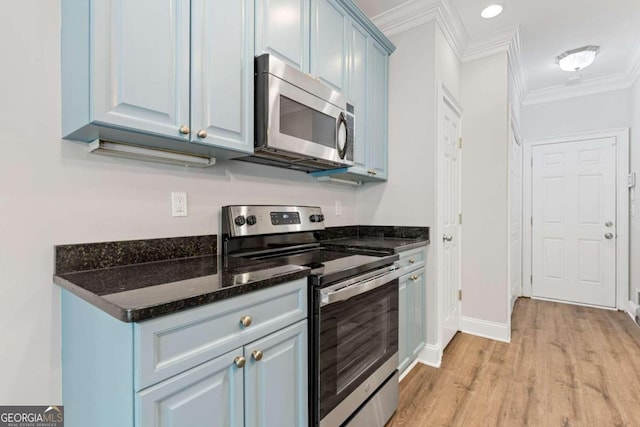 kitchen featuring blue cabinetry, dark stone counters, light wood-type flooring, appliances with stainless steel finishes, and ornamental molding