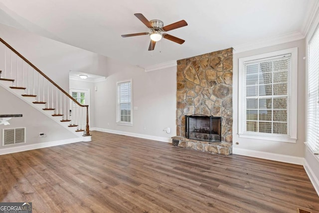 unfurnished living room featuring hardwood / wood-style floors, ceiling fan, a stone fireplace, and crown molding