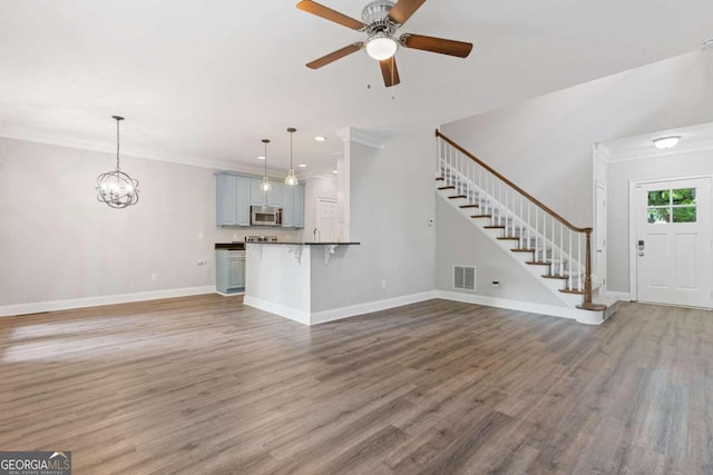 unfurnished living room with ceiling fan with notable chandelier, hardwood / wood-style flooring, and ornamental molding