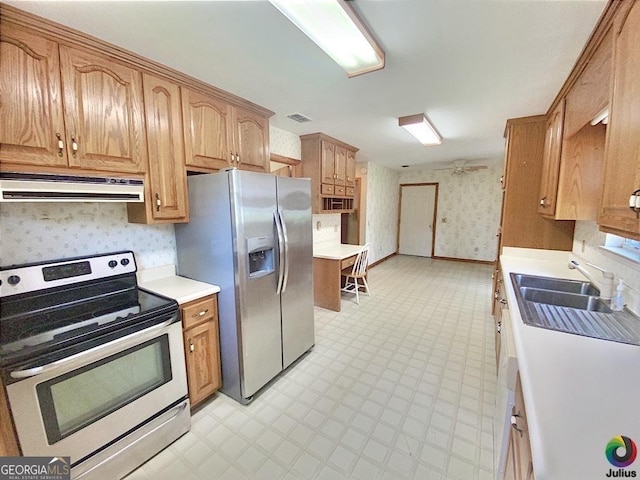 kitchen with under cabinet range hood, light countertops, appliances with stainless steel finishes, light floors, and wallpapered walls