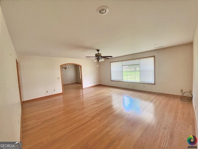 spare room with arched walkways, baseboards, ceiling fan, and light wood finished floors