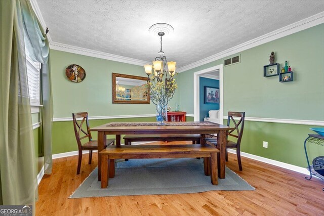 dining area with wood-type flooring, a notable chandelier, ornamental molding, and a textured ceiling