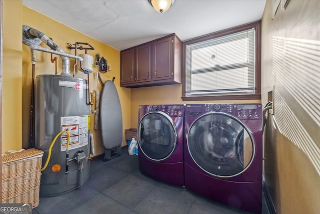 washroom featuring washing machine and clothes dryer, cabinets, water heater, and dark tile patterned floors