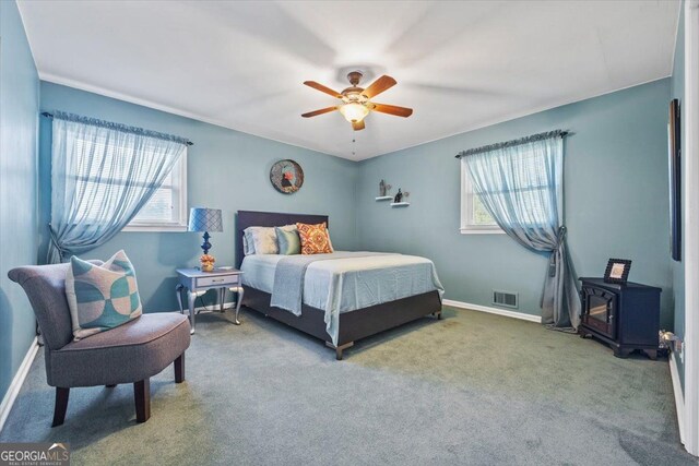 carpeted bedroom with a wood stove, multiple windows, and ceiling fan