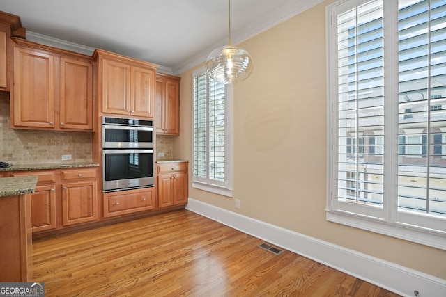 kitchen with decorative backsplash, light stone countertops, double oven, ornamental molding, and light hardwood / wood-style flooring