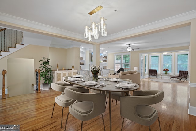 dining space with crown molding, built in shelves, ceiling fan with notable chandelier, and light hardwood / wood-style floors