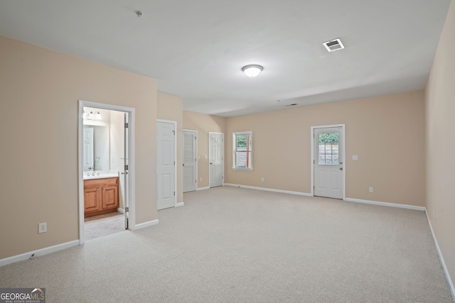 unfurnished bedroom with two closets, ensuite bathroom, and light colored carpet