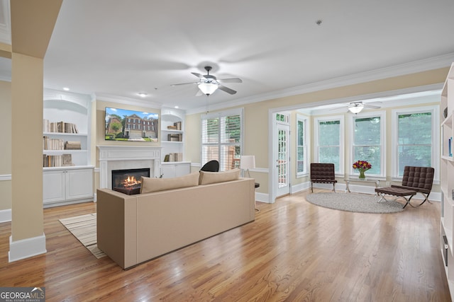 living room with light wood-type flooring, a premium fireplace, built in shelves, ornamental molding, and ceiling fan