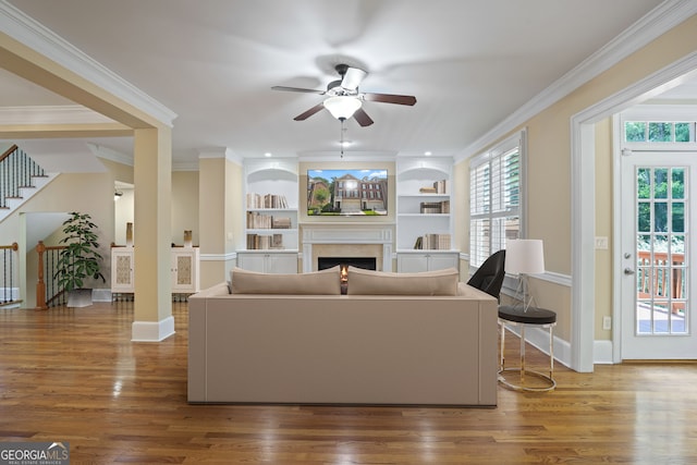 living room featuring ceiling fan, wood-type flooring, ornamental molding, and built in features