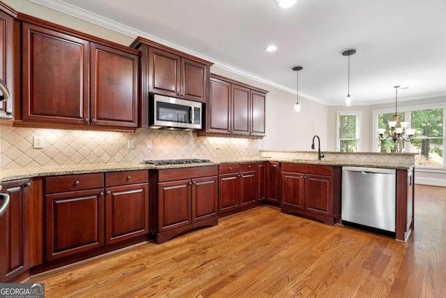 kitchen with appliances with stainless steel finishes, light hardwood / wood-style flooring, sink, hanging light fixtures, and backsplash