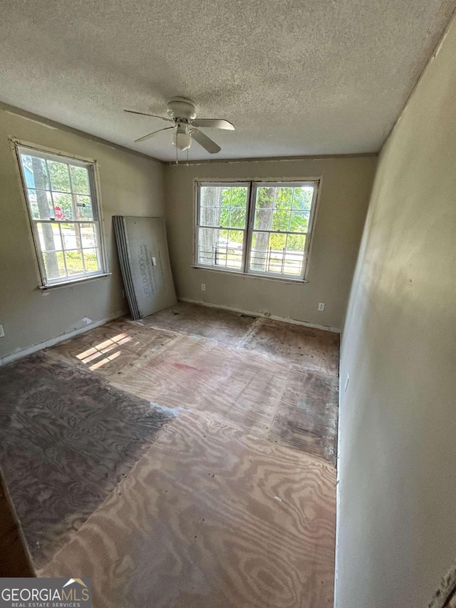 empty room featuring ceiling fan, plenty of natural light, and a textured ceiling