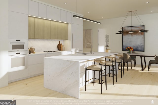 kitchen featuring white cabinetry, light hardwood / wood-style floors, sink, and a center island with sink