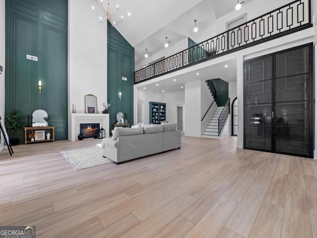 living room with light wood-type flooring, a towering ceiling, and a large fireplace