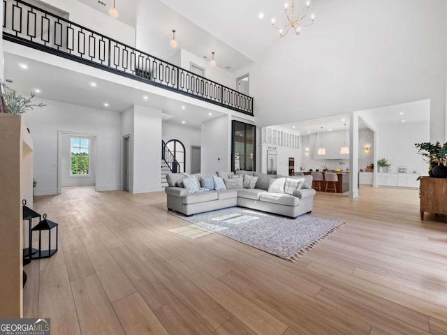 living room with light wood-type flooring, a towering ceiling, and a chandelier