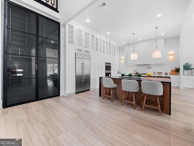 kitchen featuring a breakfast bar, light wood-type flooring, decorative light fixtures, white cabinetry, and stainless steel appliances