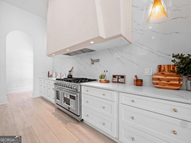 kitchen with decorative backsplash, light stone countertops, double oven range, white cabinets, and light hardwood / wood-style floors