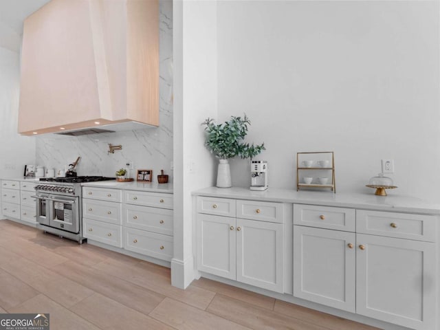 kitchen with backsplash, wall chimney exhaust hood, double oven range, light hardwood / wood-style flooring, and white cabinetry