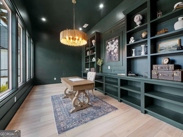 office space featuring an inviting chandelier, built in features, and light hardwood / wood-style flooring