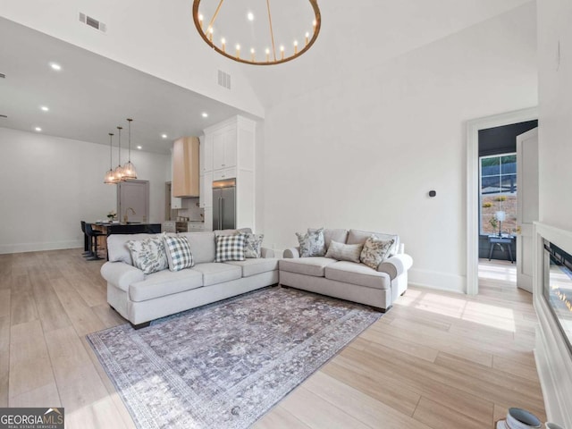 living room featuring high vaulted ceiling, a chandelier, and light hardwood / wood-style floors