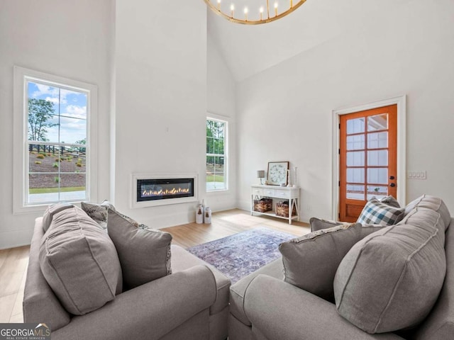 living room featuring a wealth of natural light, an inviting chandelier, high vaulted ceiling, and light wood-type flooring