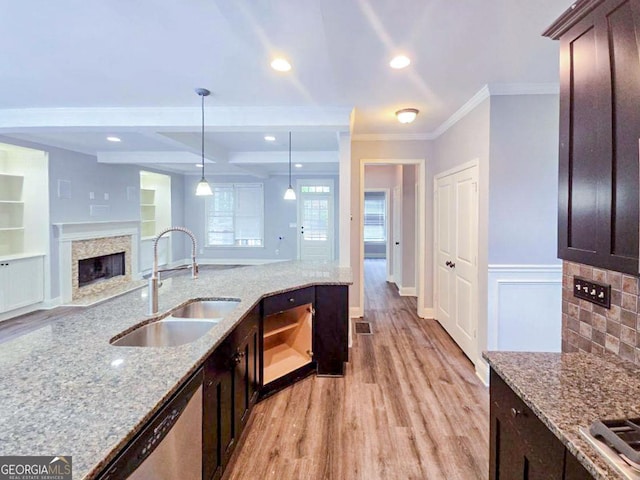 kitchen featuring decorative light fixtures, dishwasher, crown molding, light stone counters, and sink