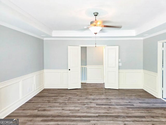 empty room with ceiling fan, dark wood-type flooring, a tray ceiling, and crown molding