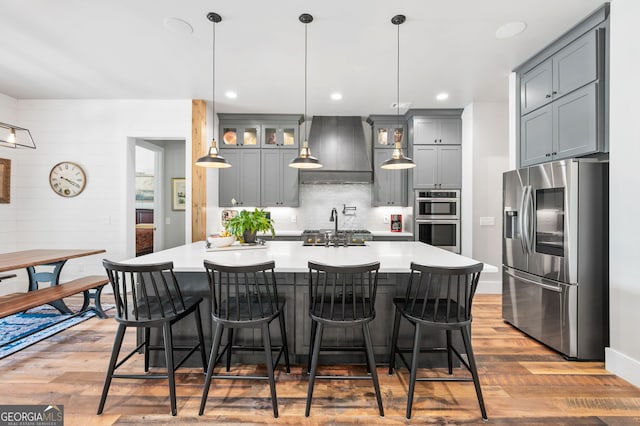 kitchen featuring tasteful backsplash, light wood-type flooring, premium range hood, stainless steel appliances, and gray cabinetry