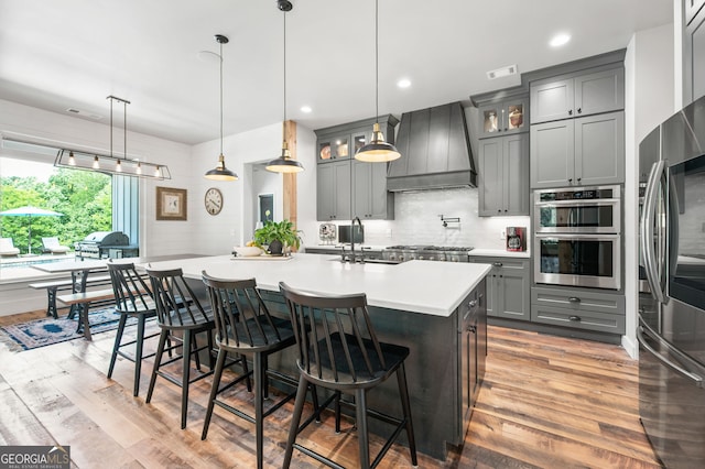 kitchen with premium range hood, appliances with stainless steel finishes, hanging light fixtures, and hardwood / wood-style floors