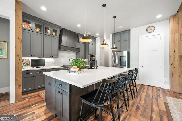 kitchen featuring stainless steel appliances, dark hardwood / wood-style flooring, an island with sink, custom range hood, and backsplash