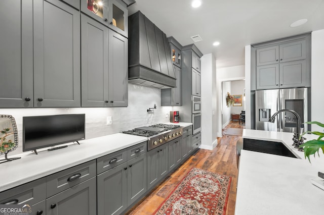 kitchen with stainless steel appliances, custom exhaust hood, decorative backsplash, wood-type flooring, and sink