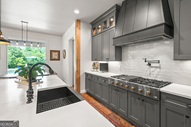 kitchen with stainless steel gas stovetop, hanging light fixtures, backsplash, and custom range hood