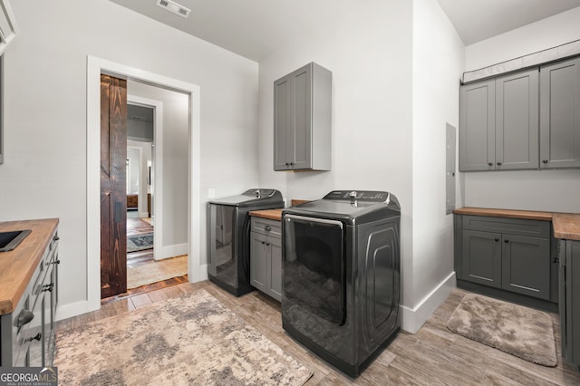 washroom with washer and clothes dryer, light hardwood / wood-style flooring, cabinets, and electric panel