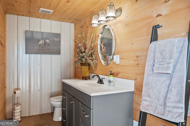 bathroom with vanity, wooden walls, and toilet