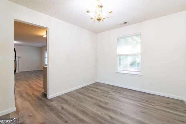 empty room featuring a textured ceiling, an inviting chandelier, and dark hardwood / wood-style flooring