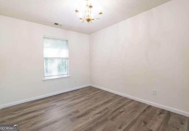 spare room featuring dark wood-type flooring, a notable chandelier, and a textured ceiling