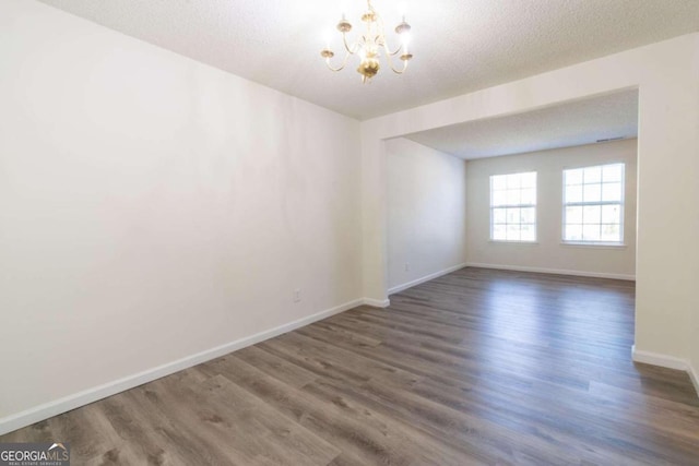 empty room featuring a textured ceiling, a chandelier, and dark hardwood / wood-style flooring