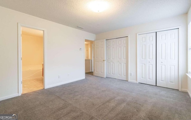 unfurnished bedroom featuring carpet, connected bathroom, multiple closets, and a textured ceiling