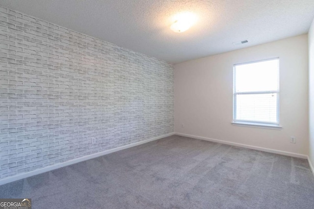 empty room with brick wall, a textured ceiling, and carpet flooring