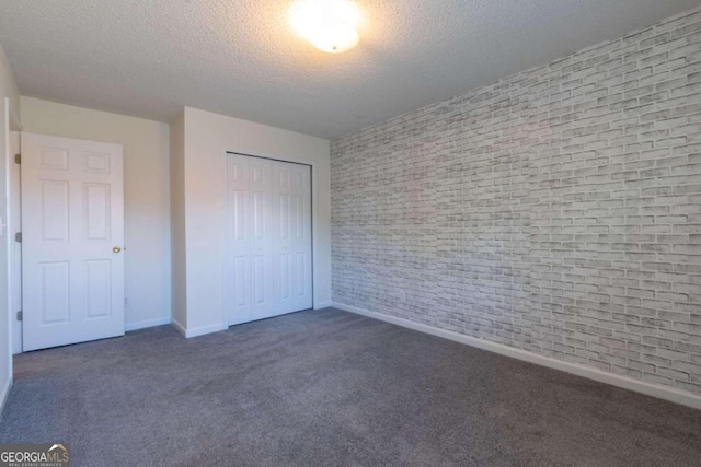 unfurnished bedroom featuring a closet, dark carpet, brick wall, and a textured ceiling