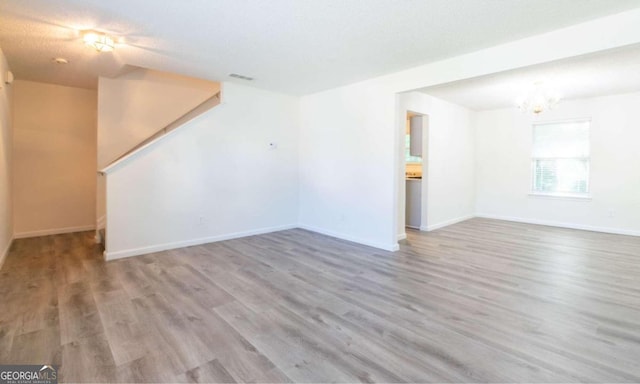 unfurnished living room with wood-type flooring, a textured ceiling, and an inviting chandelier