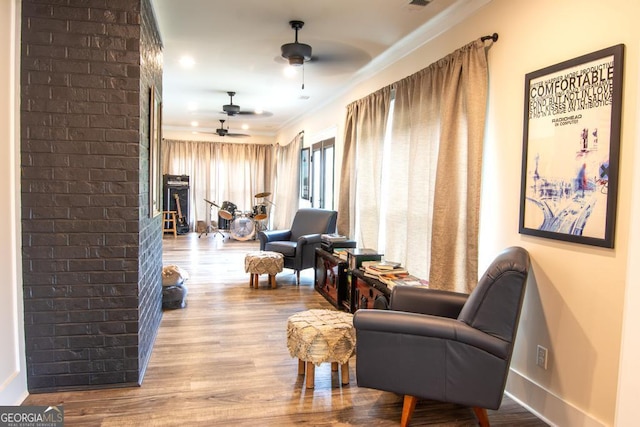 sitting room with crown molding, a fireplace, light wood finished floors, ceiling fan, and baseboards